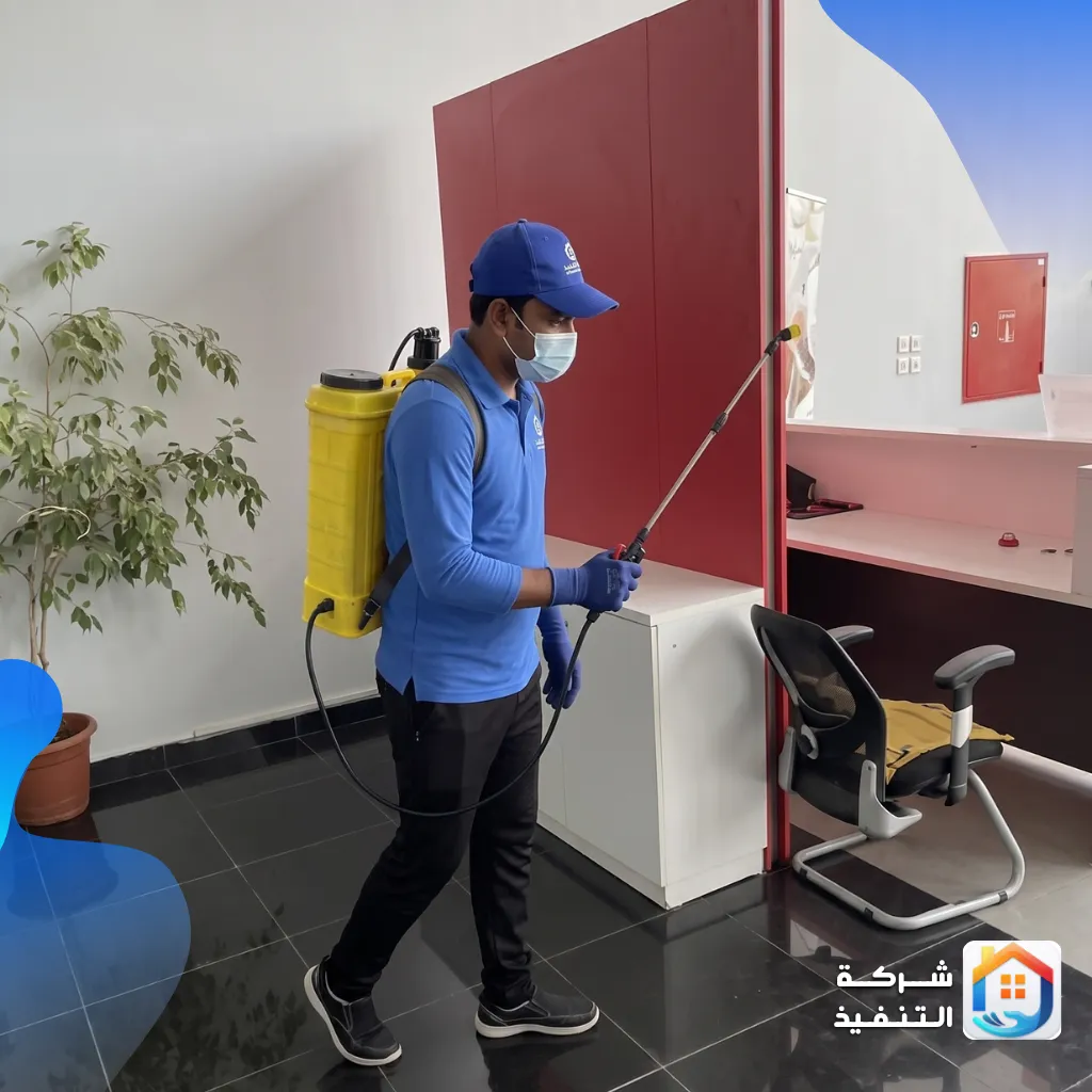 فني يرتدي زيًا أزرق وقناعًا واقيًا يقوم بعملية رش مبيدات الحشرات داخل مكتب