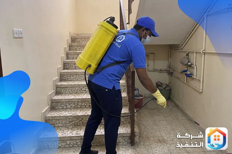 فني يرش مبيد على حافة الأرضية تحت درج عمارة سكنية بالرياض قرب عدادات المياه