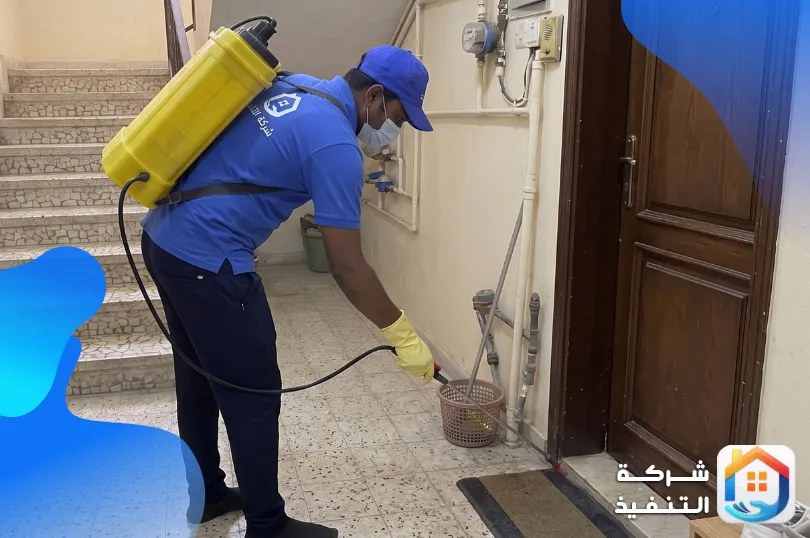 فني من افضل شركة مكافحة النمل الابيض بالرياض يرش عند حلق باب شقة وأماكن دخول المواسير في مدخل عمارة