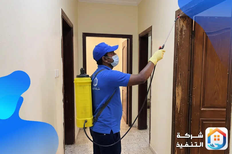 فني من شركة مكافحة النمل الابيض يرش حلق باب خشبي مصاب في ممر شقة بالرياض